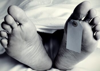 closeup of the feet of a dead body covered with a sheet, with a blank tag tied on the big toe of his left foot, in monochrome, with a vignette added