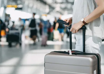 Cropped image of young woman holding passport and suitcase walking in the international airport hall