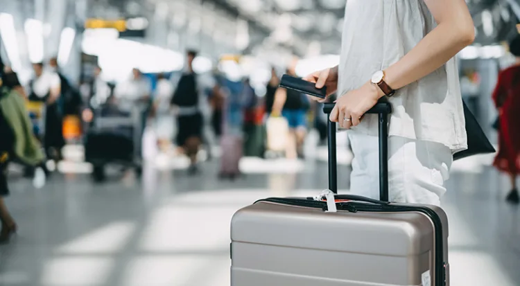 Cropped image of young woman holding passport and suitcase walking in the international airport hall