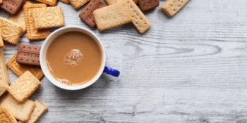 A British biscuit and shortbread selection arranged on a wooden board as a border background with a cup of tea