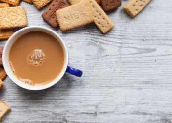 A British biscuit and shortbread selection arranged on a wooden board as a border background with a cup of tea