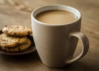 Cup of coffee with milk and cookies with chocolate pieces on the brown wooden table. Resting and enjoying time with coffee and sweets. Drink and snack concept.