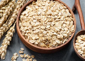 Oat flakes or rolled oats in wooden bowl on concrete table background. Healthy eating concept