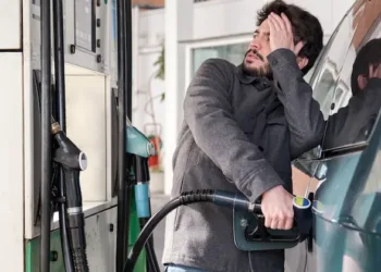 Young man refueling his vehicle while looking worried at the high gas prices at a gas station.