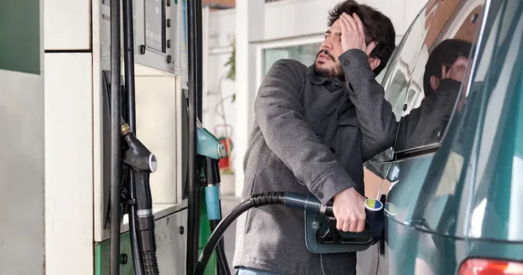 Young man refueling his vehicle while looking worried at the high gas prices at a gas station.