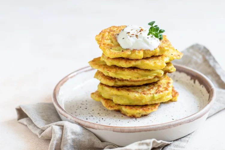 Stack of vegetable fritters or pancakes with yoghurt or cream sour dressing and herbs. Cabbage or zucchini fritters on ceramic plate. Healthy vegetarian food. Selective focus.