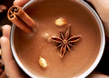 Hands holding a mug of hot chocolate with chai spices like cinnamon, cardamon, cloves, star anise as a sweet warm winter dessert drink