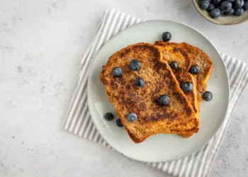 Flat lay of three slices of french toast with blueberries on a plate on grey background, copy space on the left, minimalistic style