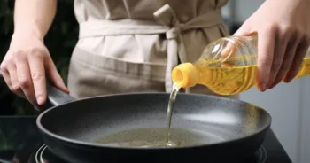 Woman pouring cooking oil from bottle into frying pan, closeup