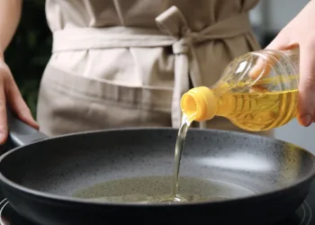 Woman pouring cooking oil from bottle into frying pan, closeup