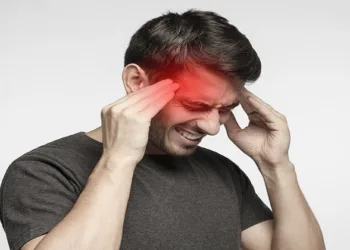 Closeup of young man touching temples with fingers as if suffering from severe migraine, feeling sick, isolated on gray background