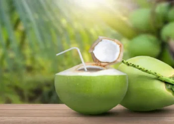 Coconut juice (coconut water) and fresh young green coconut with coco nut tree blurred background.