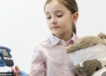 Doctor checking diabetics on equipment of girl with teddybear at clinic