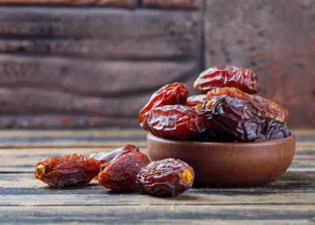 Sweet dates in a clay plate on stone tile and wooden background, side view.