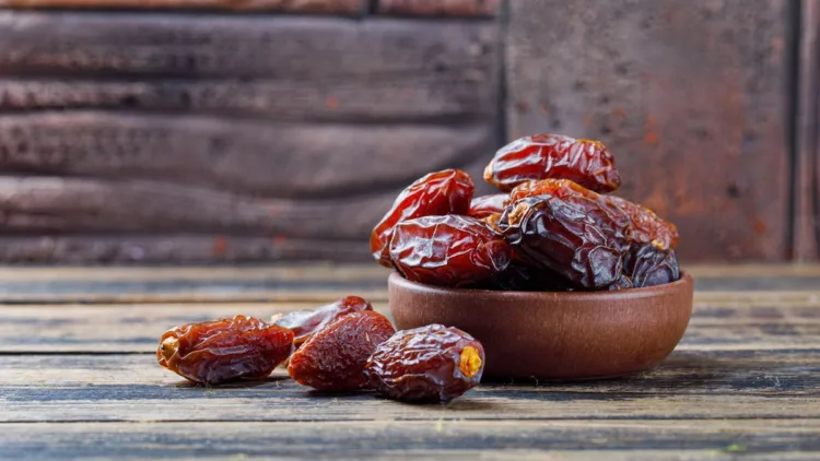 Sweet dates in a clay plate on stone tile and wooden background, side view.