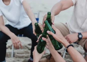 hands holding beverage bottles and touching each other at a party.