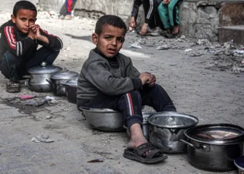 TOPSHOT - Boys sit with empty pots as displaced Palestinians queue for meals provided by a charity organisation ahead of the fast-breaking "iftar" meal during the Muslim holy month of Ramadan, in Rafah in the southern Gaza Strip on March 16, 2024, amid the ongoing conflict in the Palestinian territory between Israel and the militant group Hamas. (Photo by SAID KHATIB / AFP) (Photo by SAID KHATIB/AFP via Getty Images)