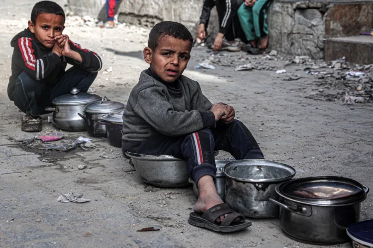 TOPSHOT - Boys sit with empty pots as displaced Palestinians queue for meals provided by a charity organisation ahead of the fast-breaking "iftar" meal during the Muslim holy month of Ramadan, in Rafah in the southern Gaza Strip on March 16, 2024, amid the ongoing conflict in the Palestinian territory between Israel and the militant group Hamas. (Photo by SAID KHATIB / AFP) (Photo by SAID KHATIB/AFP via Getty Images)