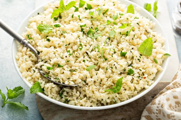 Cauliflower rice with herbs and lemon juice in a white bowl, healthy low carb trendy side dish recipe