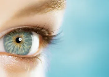 Closeup on the opened blue eye of a young woman 23 years old, blue background, empty space on right, high section, France